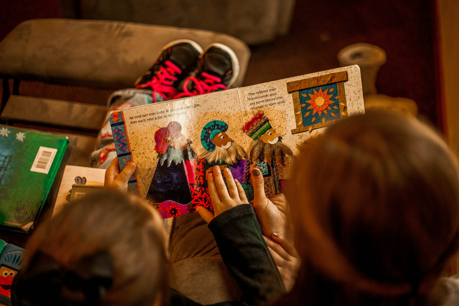 Two school-age children reading a book together on a sofa